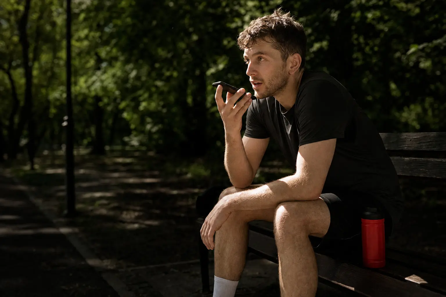 A person on a park bench after a run, speaking to their phone.